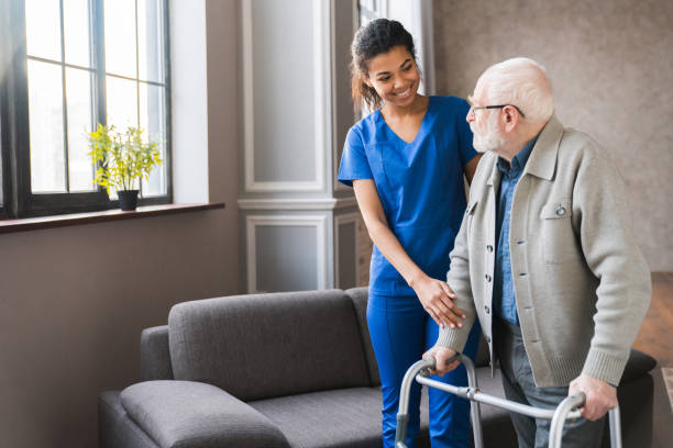 A caring nurse helping an elderly man walk with a walker at home